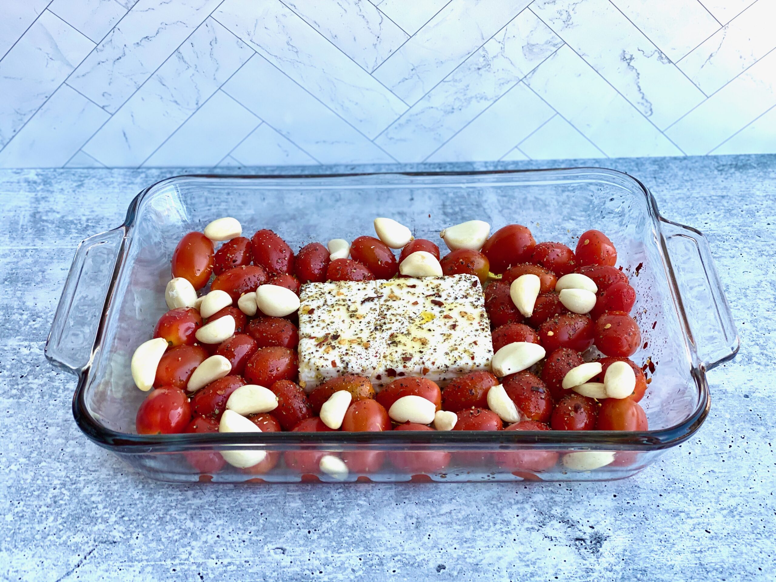 Image of feta cheese in a baking dish with tomatoes and whole cloves of garlic