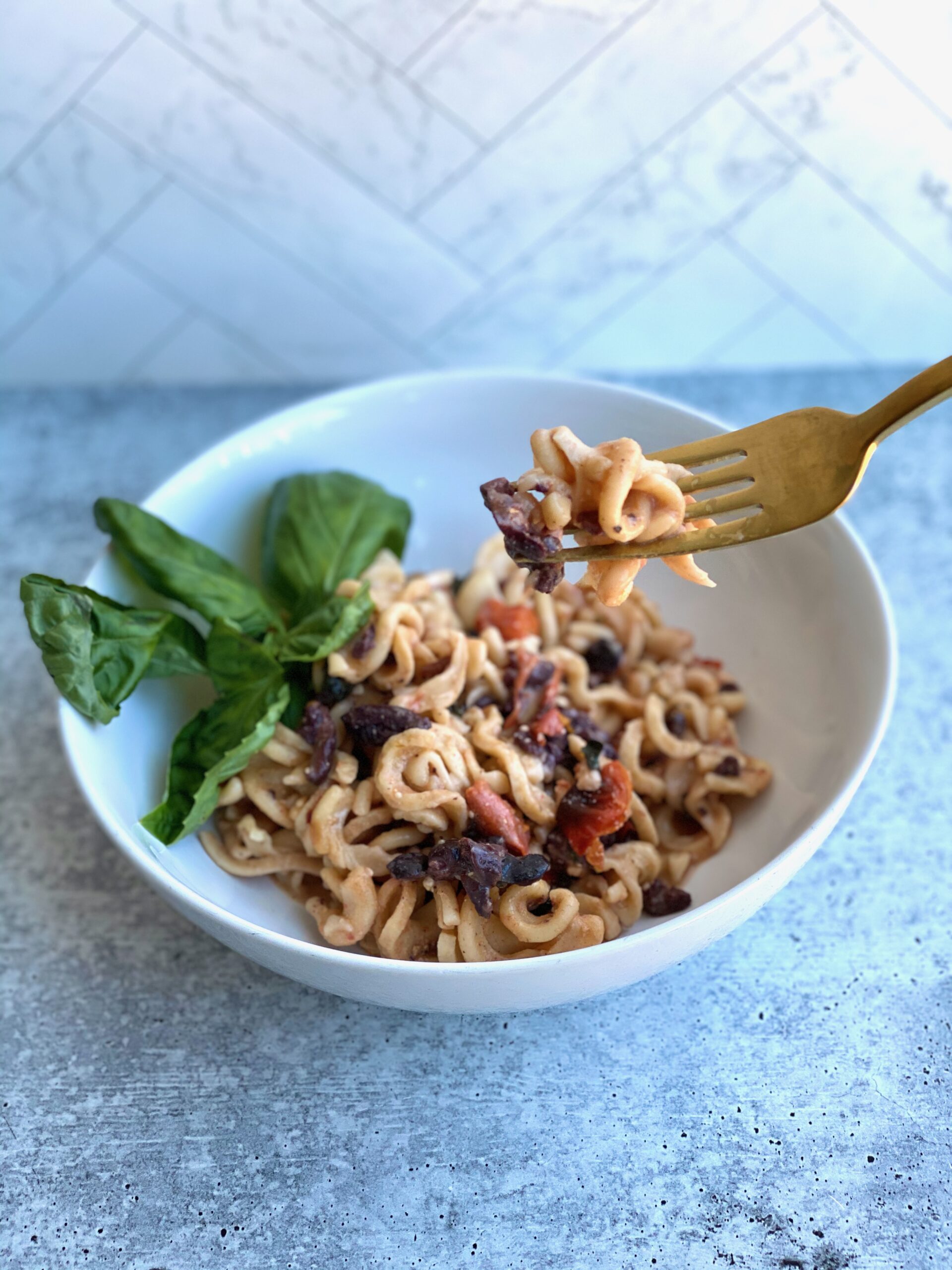 Image of a bite of pasta on a fork with the bowl of pasta behind it