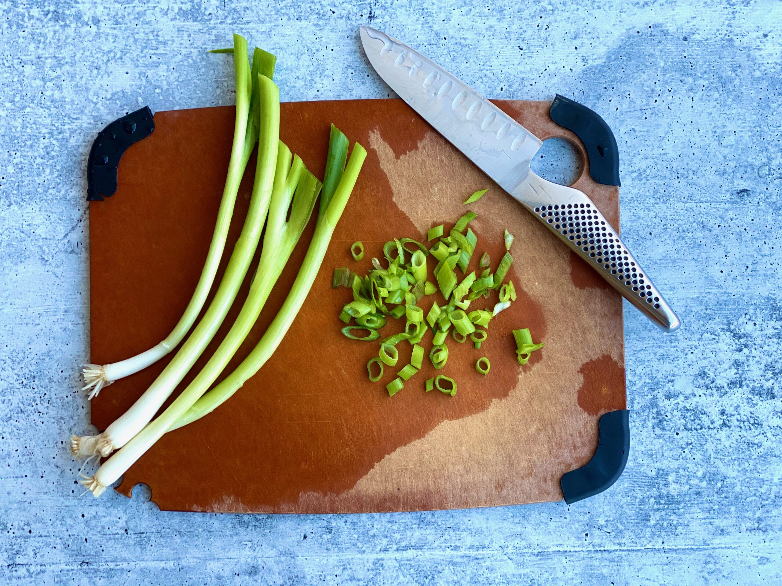 An image of scallions half chopped on a cutting board with a knife