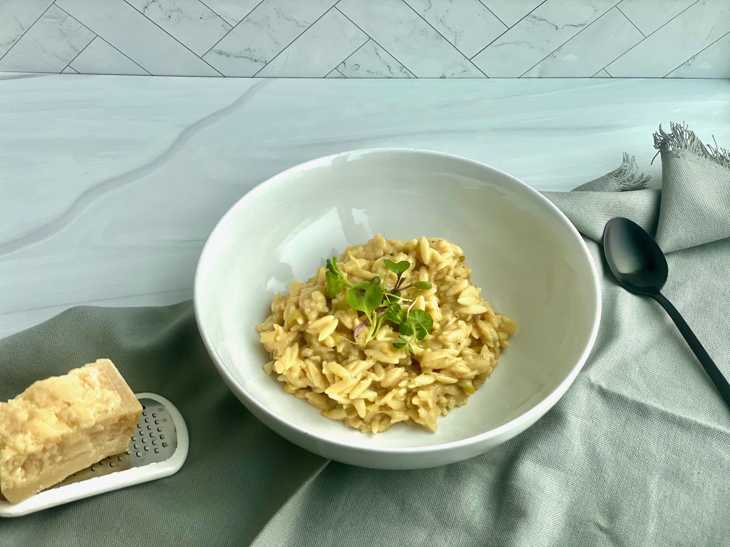 An image of a bowl of orzo with a rind of parmesan cheese and a spoon