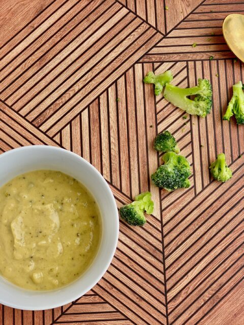 Image of a bowl of soup with pieces of broccoli and a spoon in the background