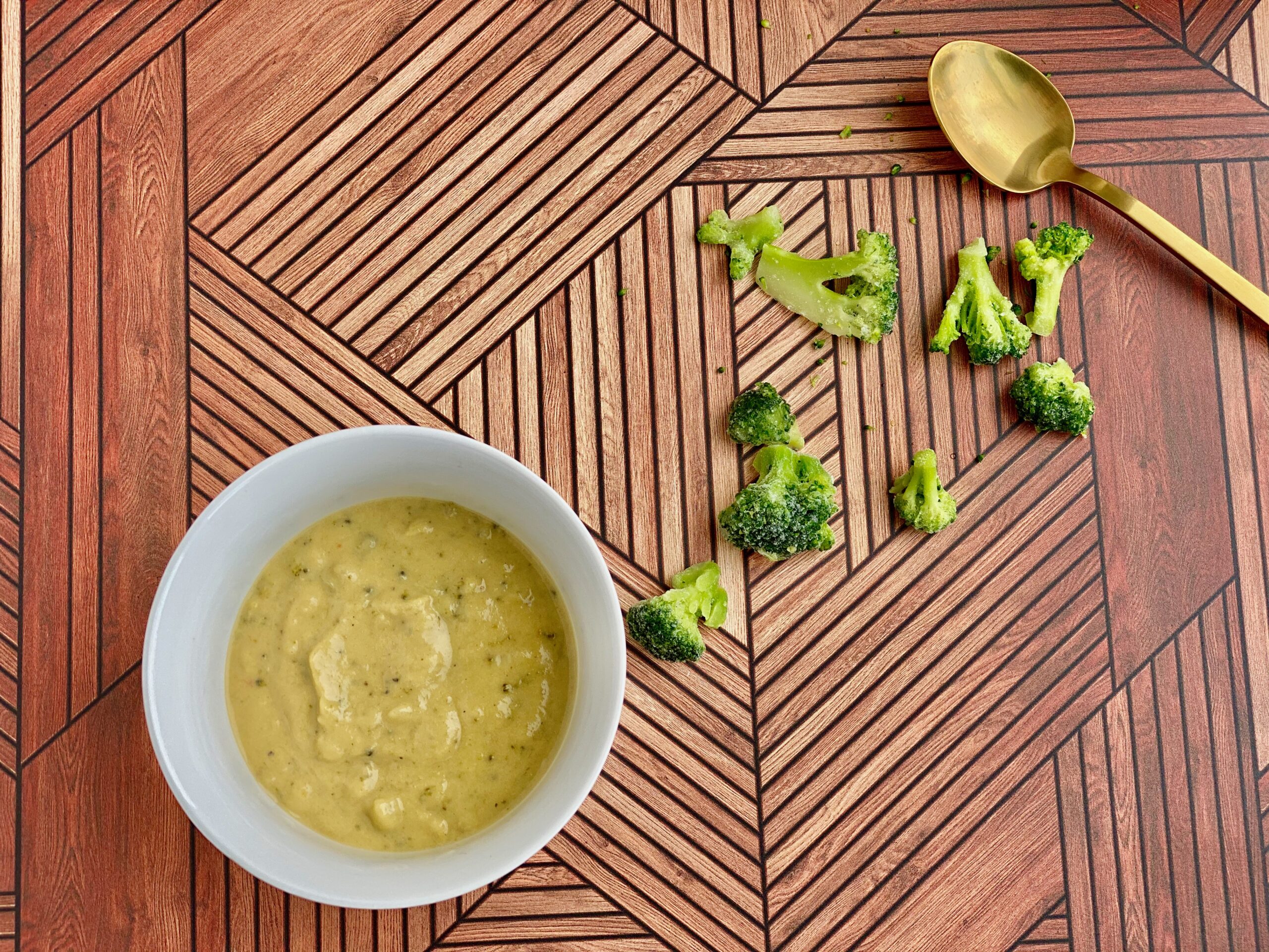 Image of a bowl of soup with pieces of broccoli and a spoon in the background
