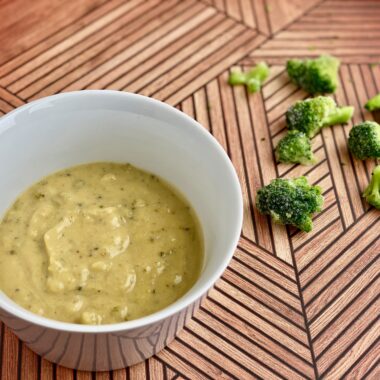 Image of a bowl of soup with pieces of broccoli in the background