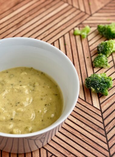 Image of a bowl of soup with pieces of broccoli in the background