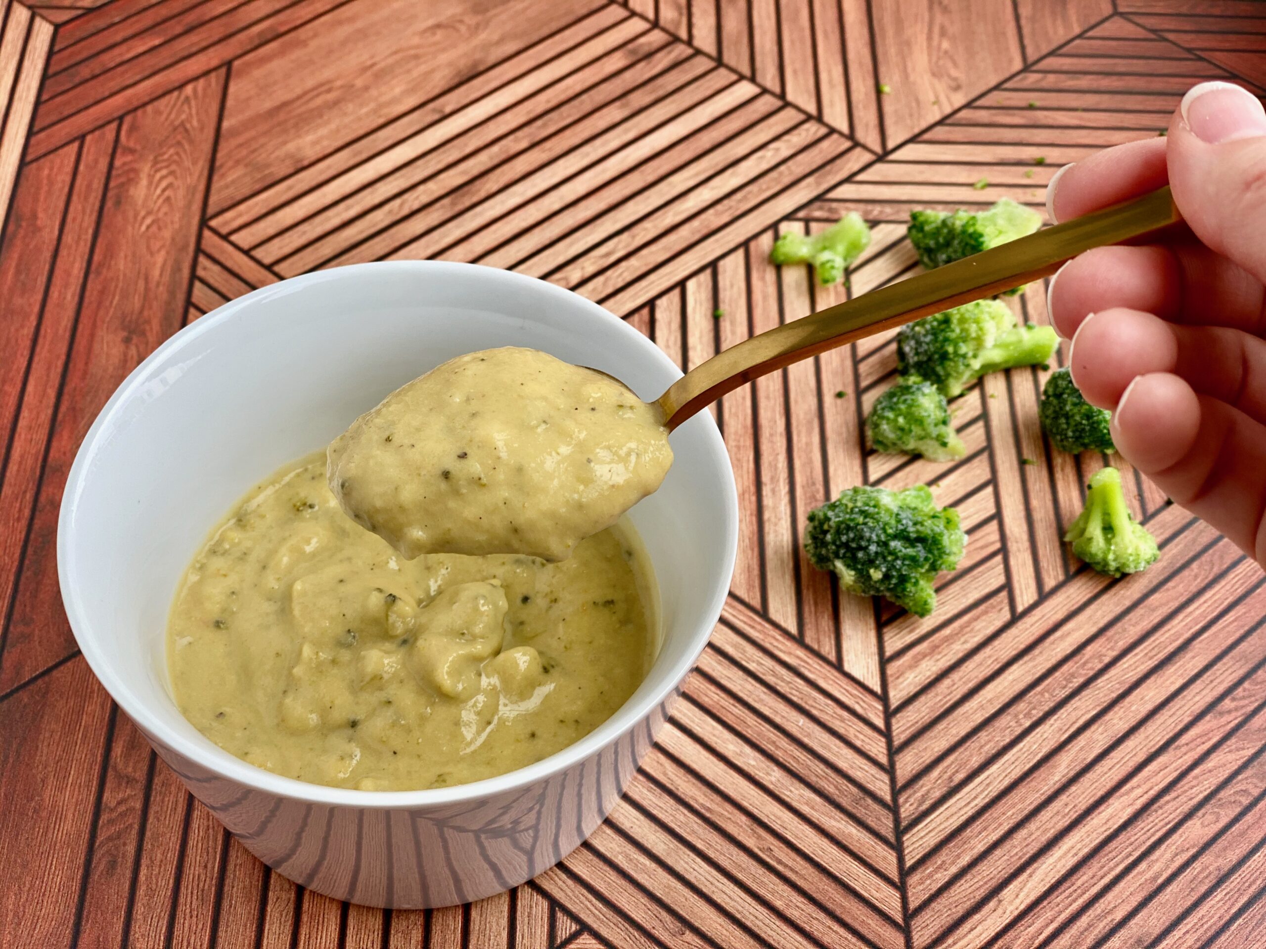 Image of a bowl of soup with a bite on a spoon and broccoli in the background