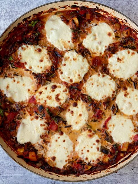 An image of a pan full of vegetables with baked, bubbly cheese on top