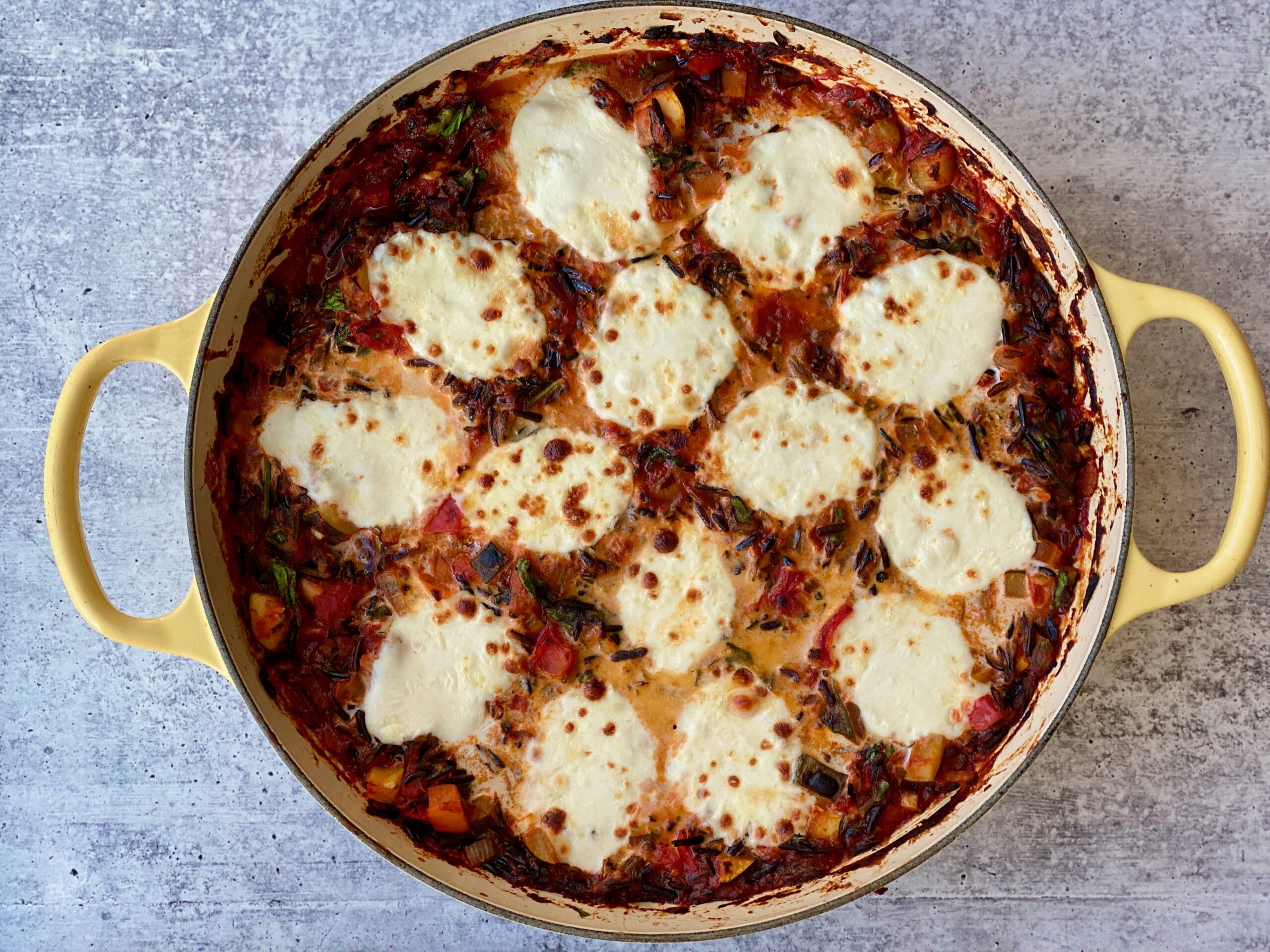 An image of a pan full of vegetables with baked, bubbly cheese on top