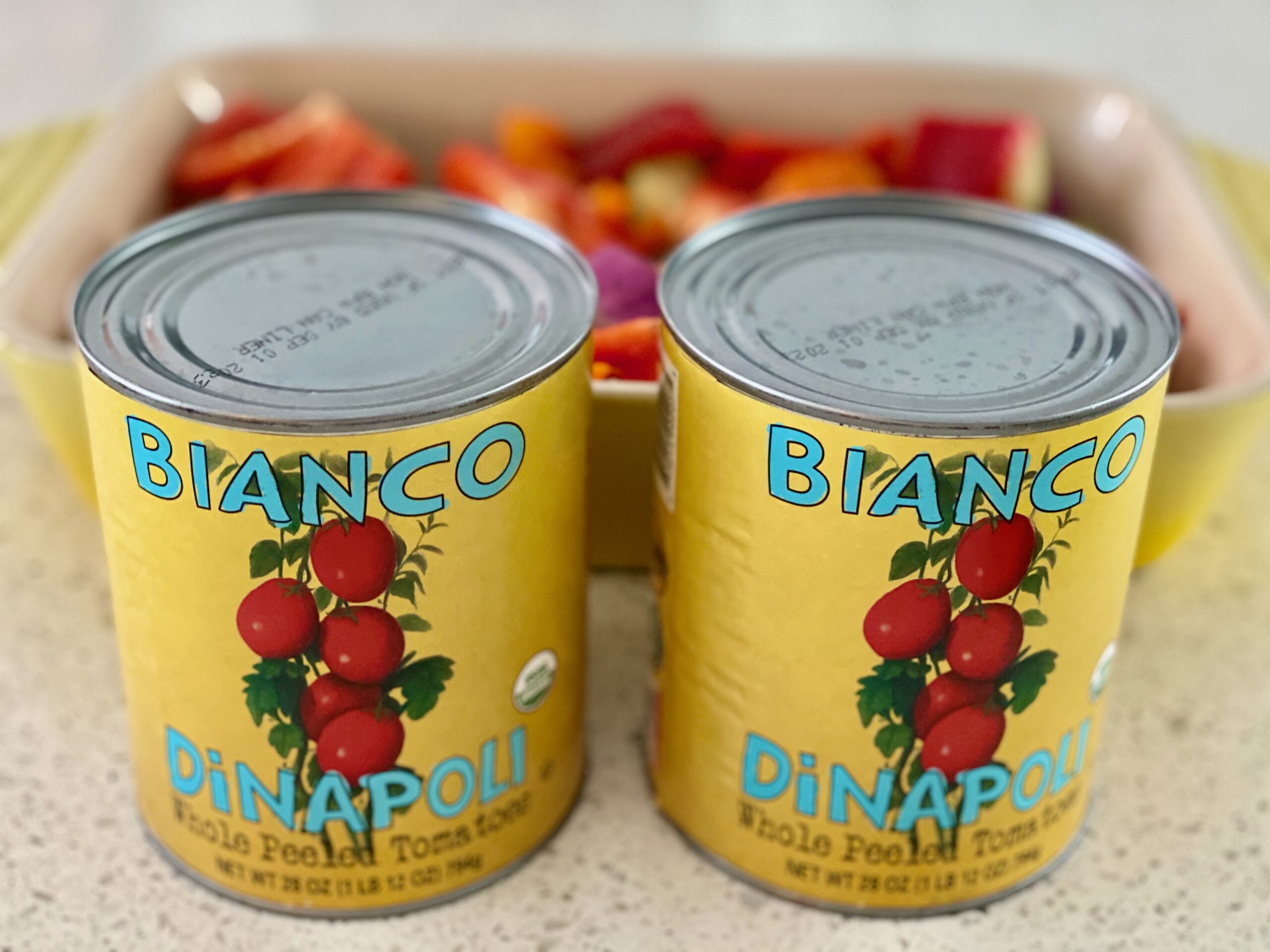 An image of two cans of tomatoes with a pan of vegetables in the background