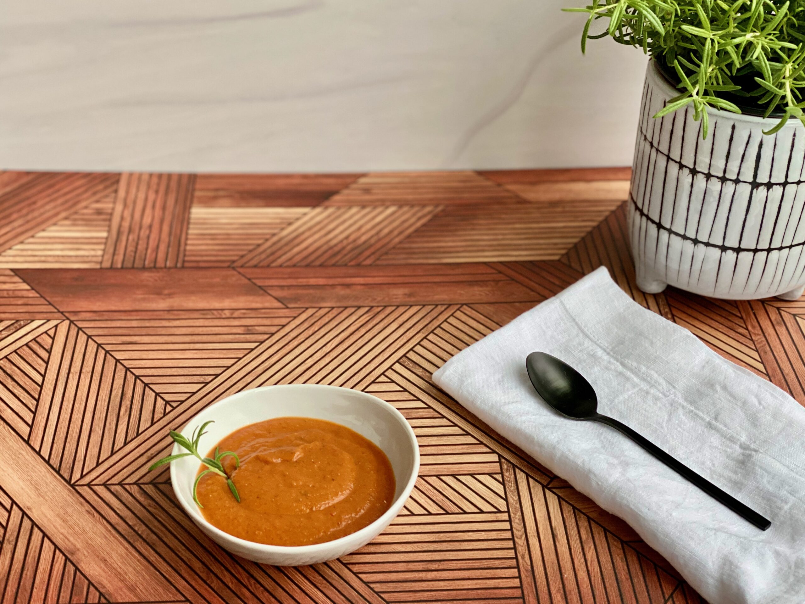 An image of a bowl of tomato soup with a rosemary plant in the background