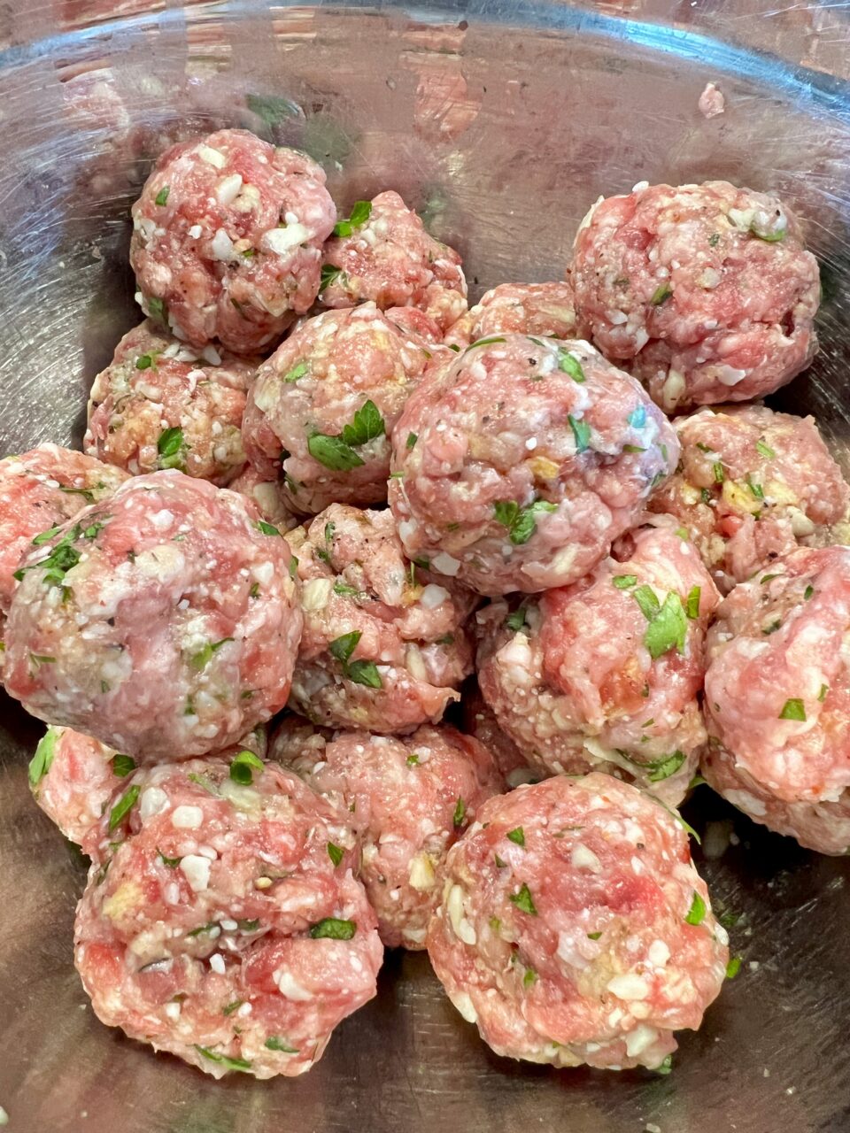 A metal bowl filled with raw meatballs