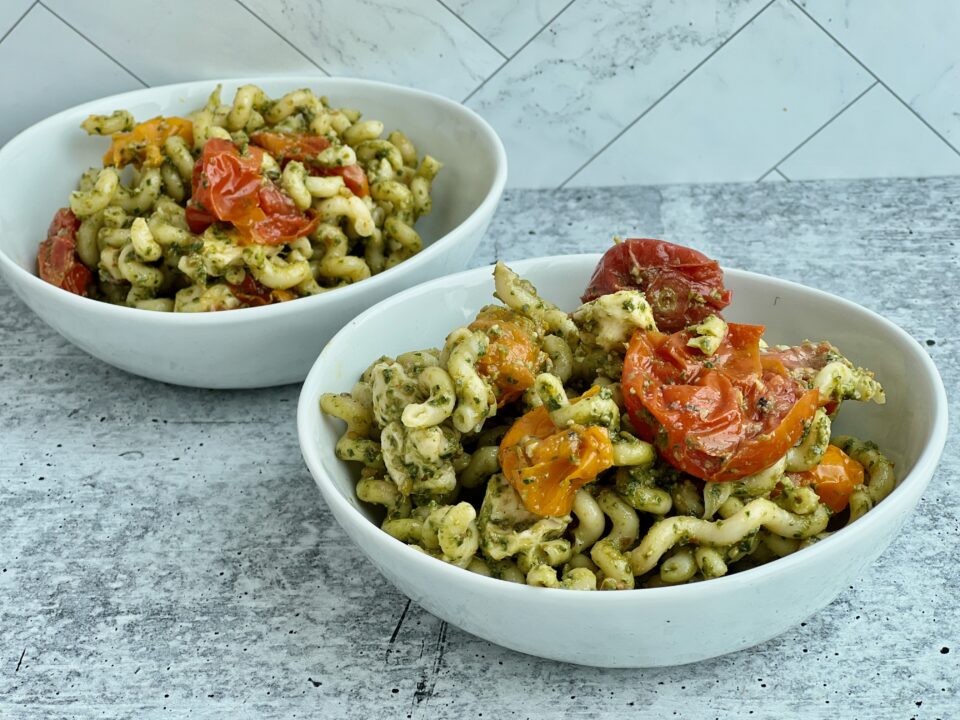 Two bowls of pesto pasta with roasted tomatoes in it