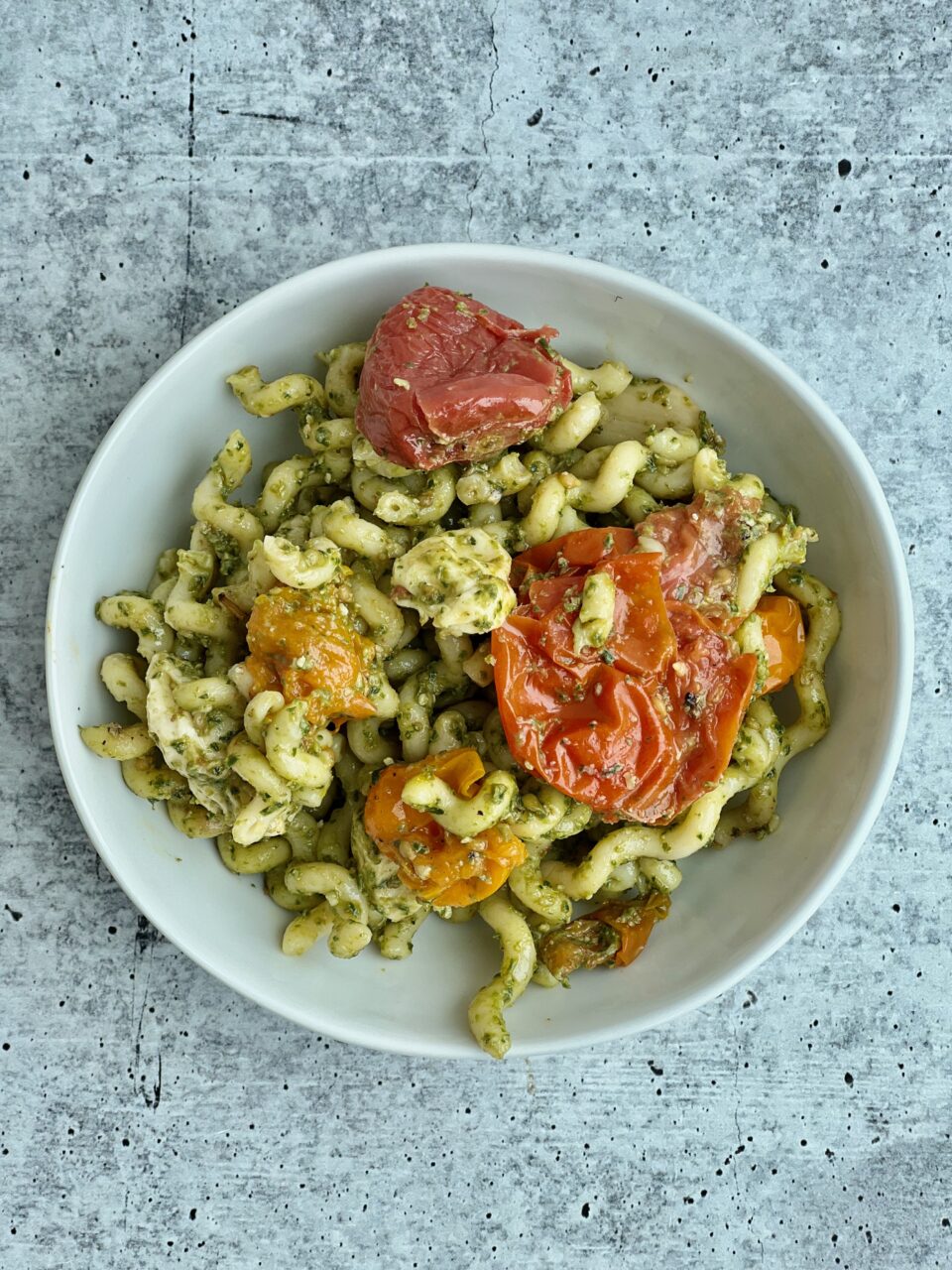 A bowl of pesto pasta with roasted tomatoes in it