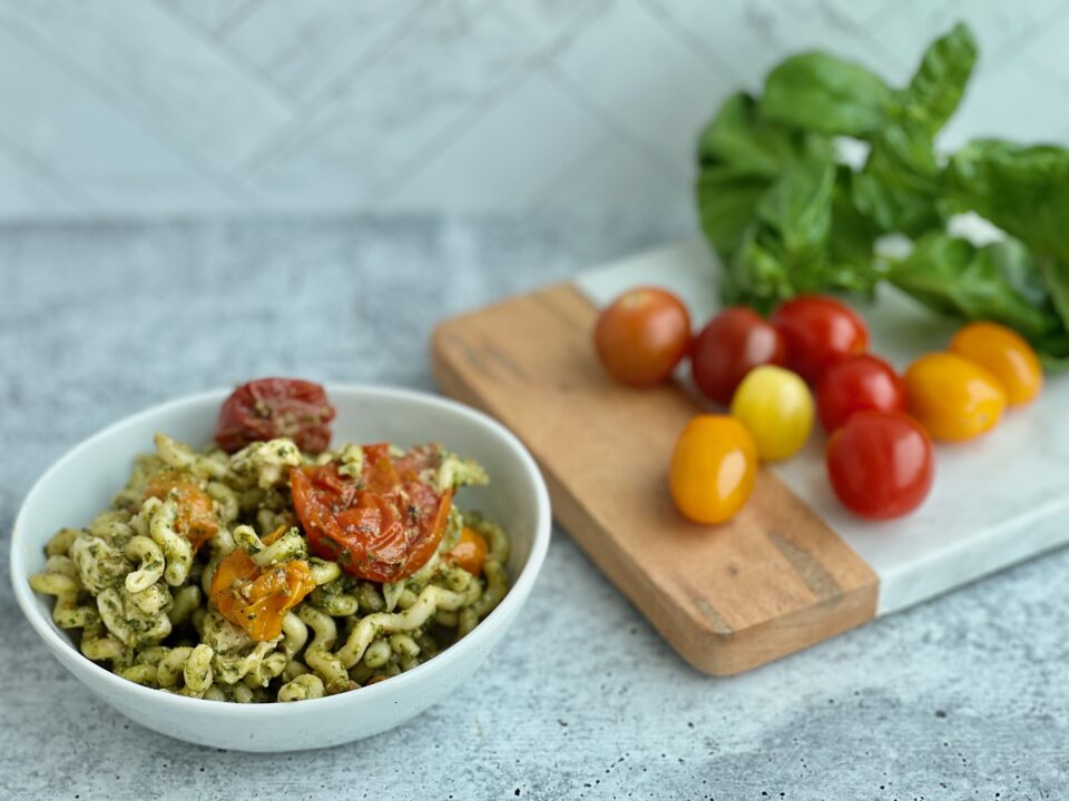 A bowl of pesto pasta with roasted tomatoes in it