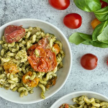 A bowl of pesto pasta with roasted tomatoes in it