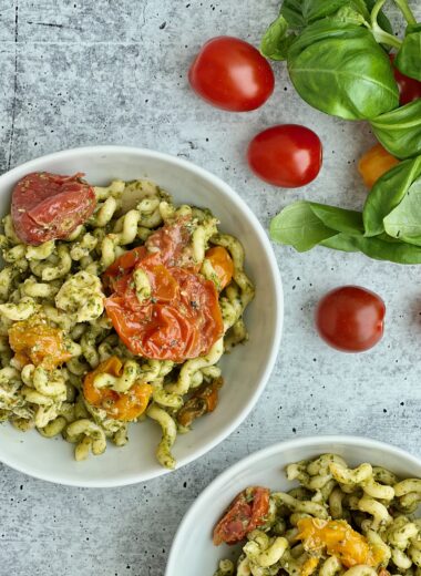 A bowl of pesto pasta with roasted tomatoes in it