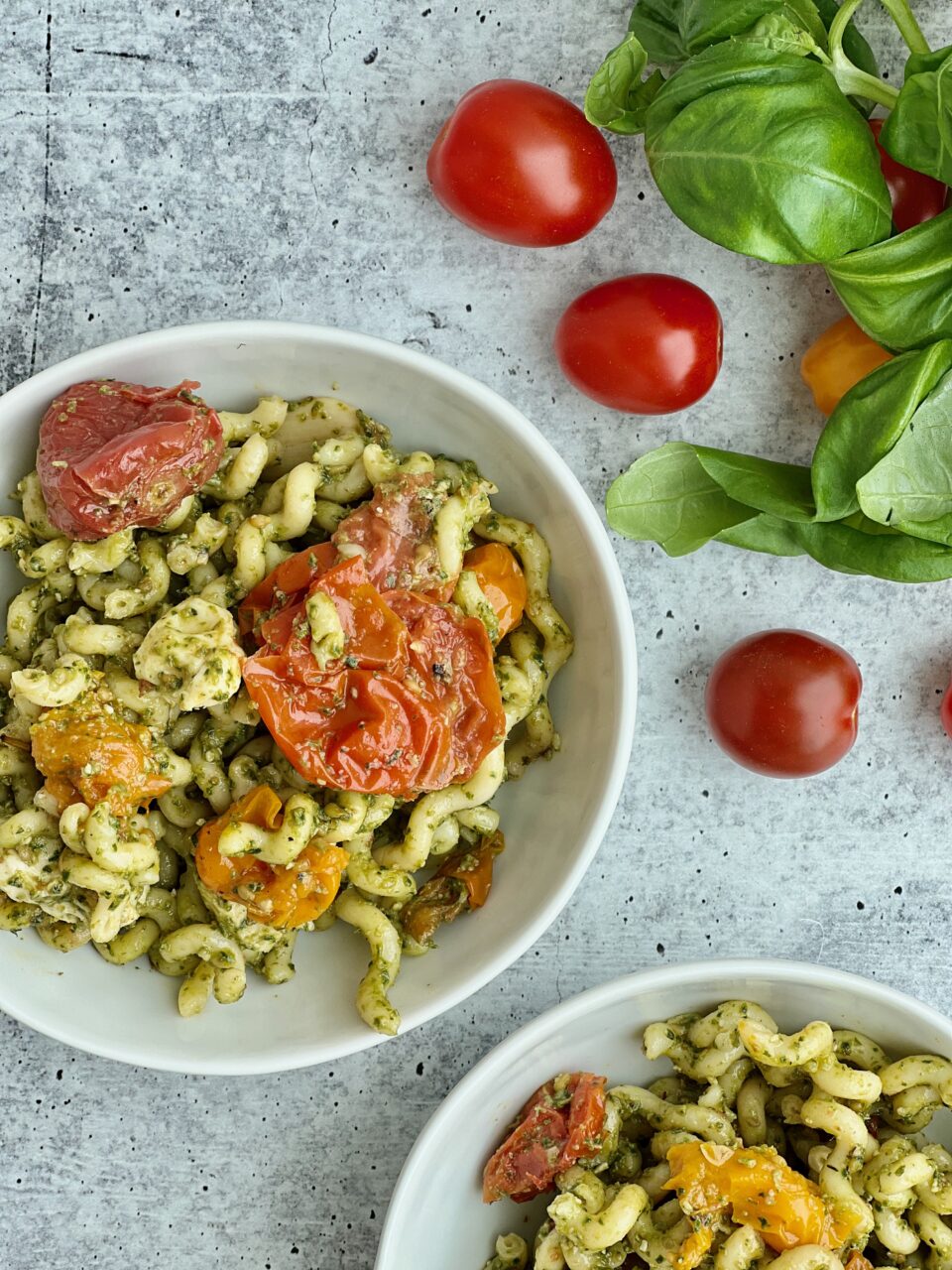 A bowl of pesto pasta with roasted tomatoes in it