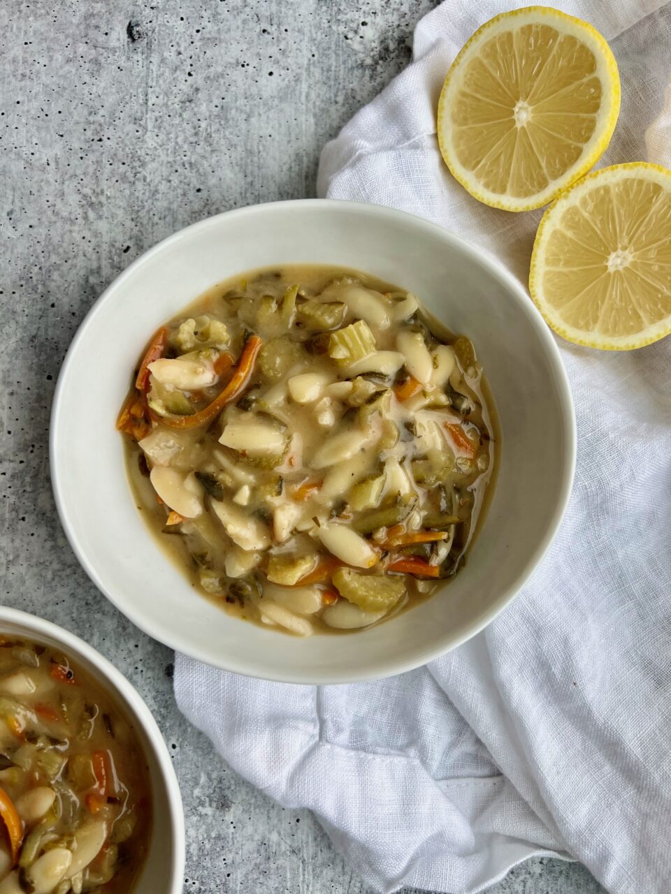 A bowl of lemon orzo soup with lemons in the background