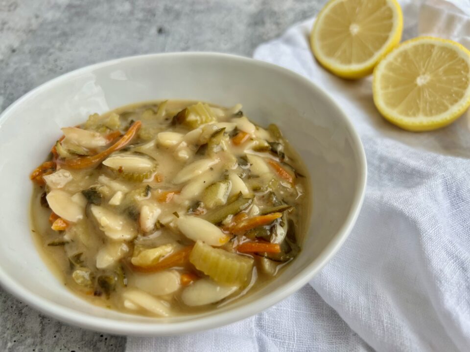 A bowl of lemon orzo soup with lemons in the background