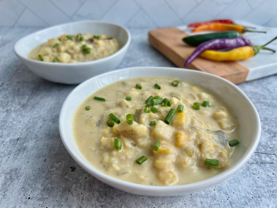 Two bowls of corn poblano chowder with chili peppers in the background