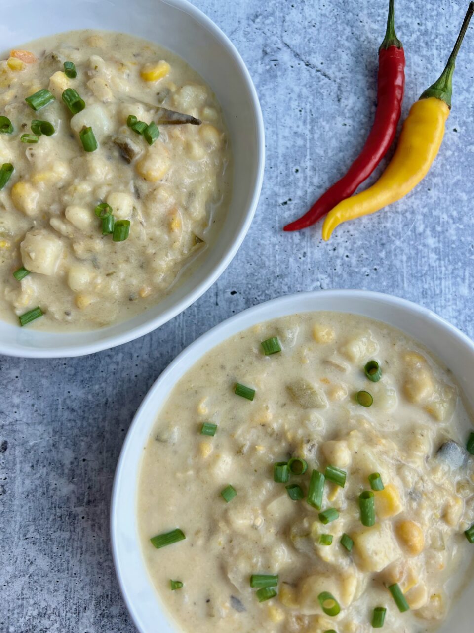 A picture of two bowls of corn poblano chowder with chili peppers in background