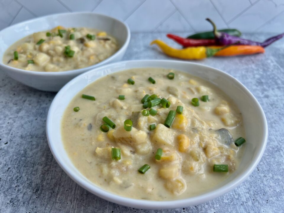 Two bowls of corn poblano soup with chilis in the background